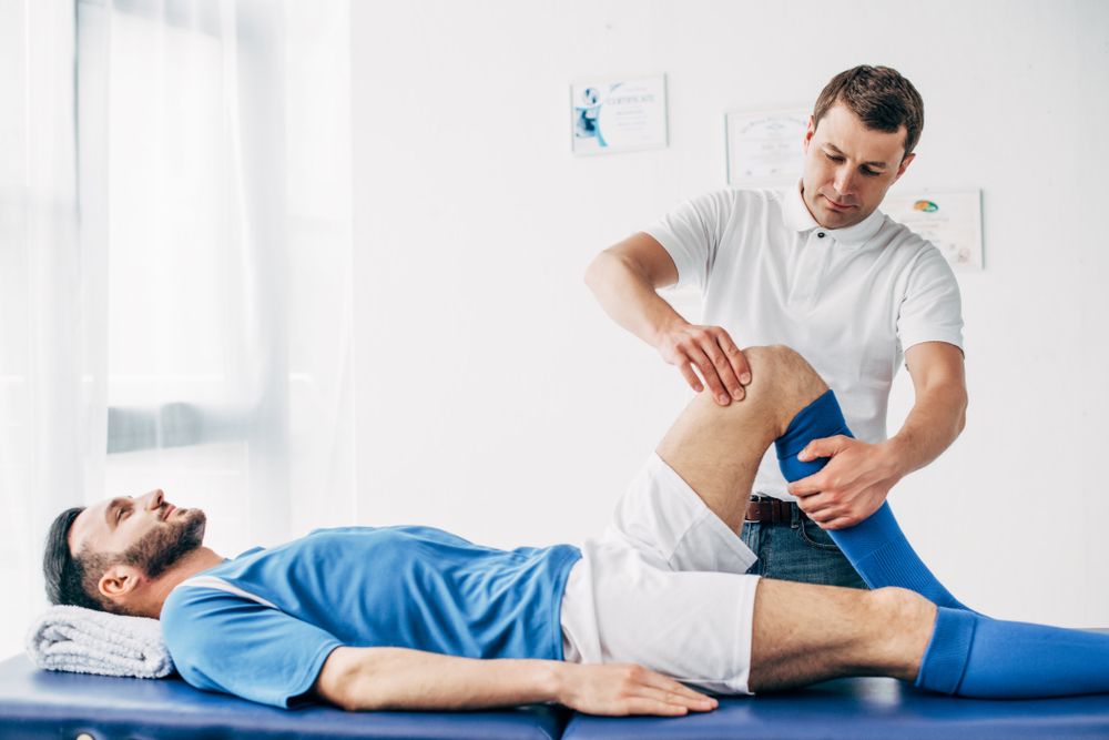 Handsome,Physiotherapist,Massaging,Leg,Of,Football,Player,In,Hospital